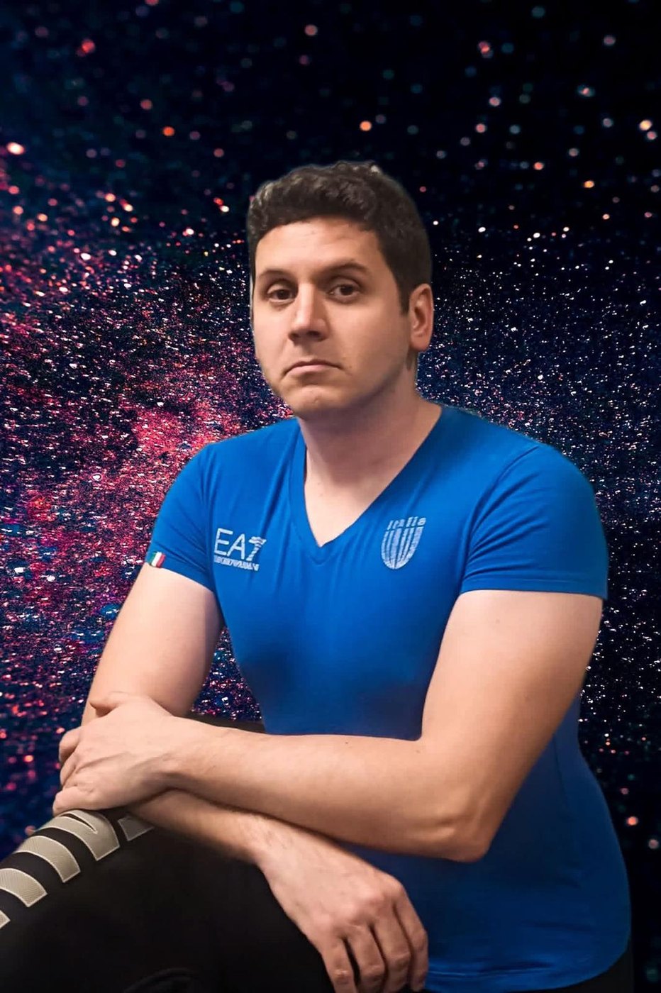 Christian Consalvi a braccia conserte con maglietta blu EA7 e bandierina italiana su sfondo stellato rosa e blu